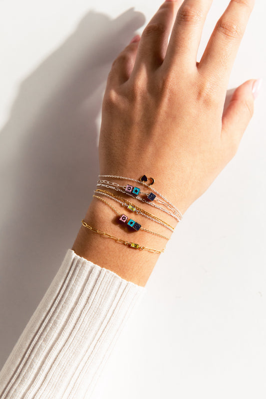 A person's wrist showcasing multiple bracelets with various charms, including hearts and flowers, in gold and silver colors.